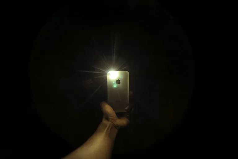 Seseorang menggunakan telefon pintar dalam bilik gelap, skrin menerangi tangannya
